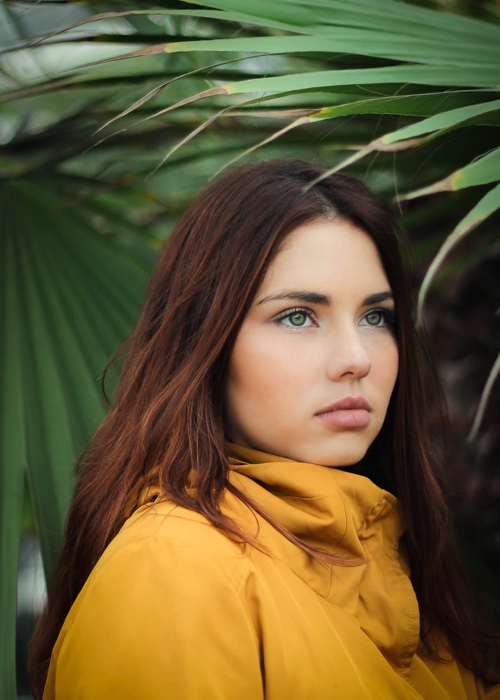 A portrait of Willow in a yellow jacket with plants in the background.